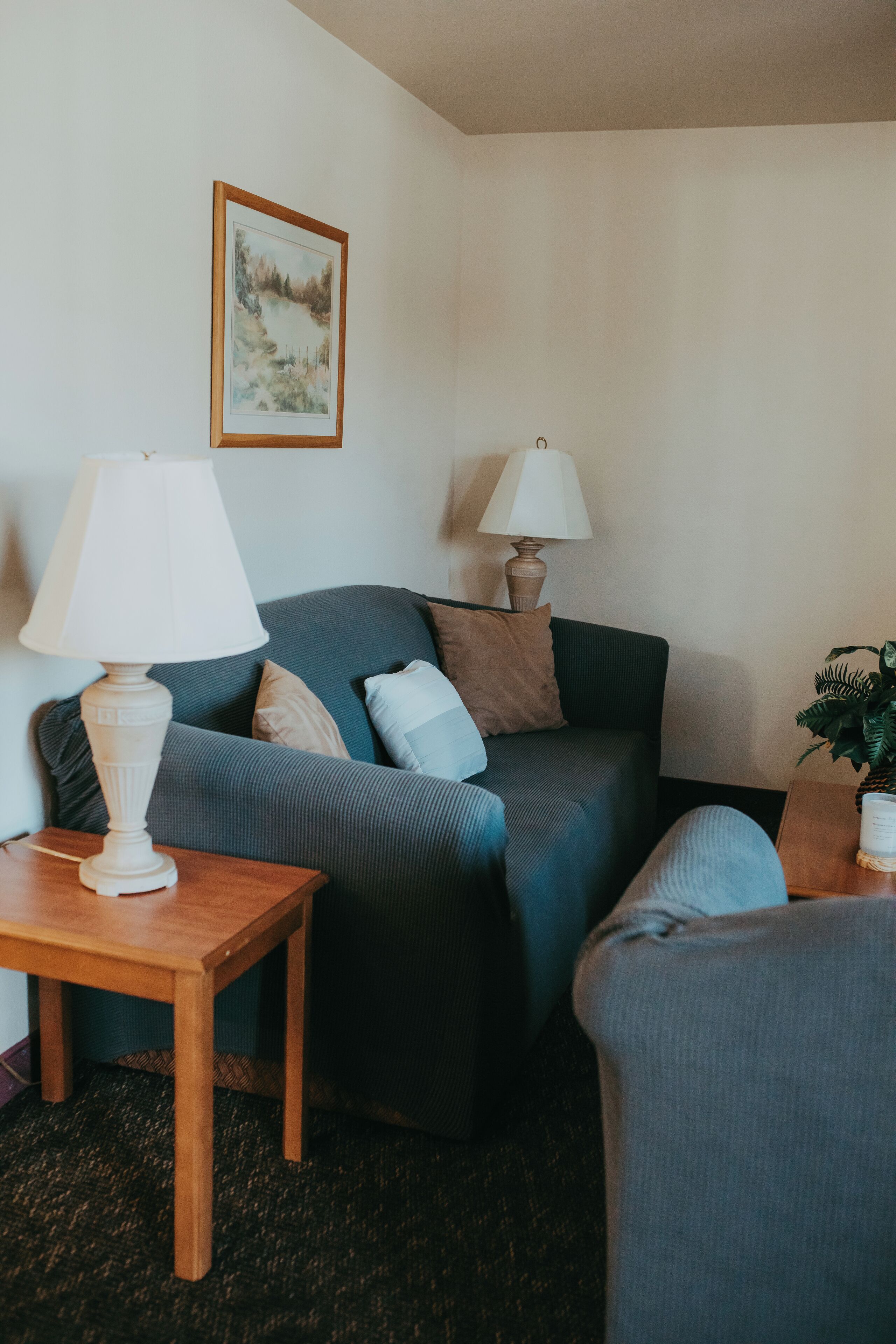 A living room with a blue sofa, a wooden side table, a lamp, and a framed picture on the wall.