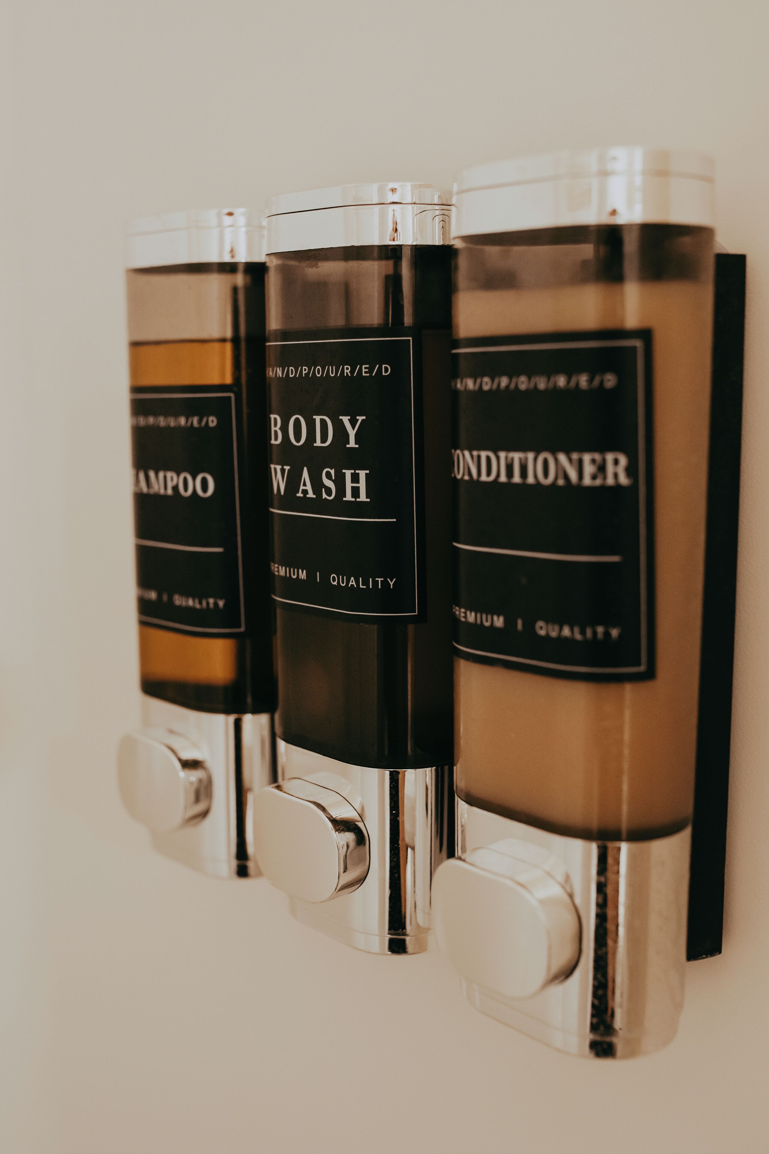 Tres botellas de gel de baño, champú y acondicionador colgadas en una pared.