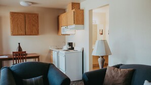 Un espace de vie compact comprenant un coin cuisine, un coin repas et un espace détente avec un canapé et des fauteuils.
