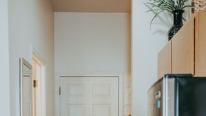 Un couloir étroit, avec une porte blanche fermée au fond, un sol recouvert de moquette et un réfrigérateur noir sur la droite.