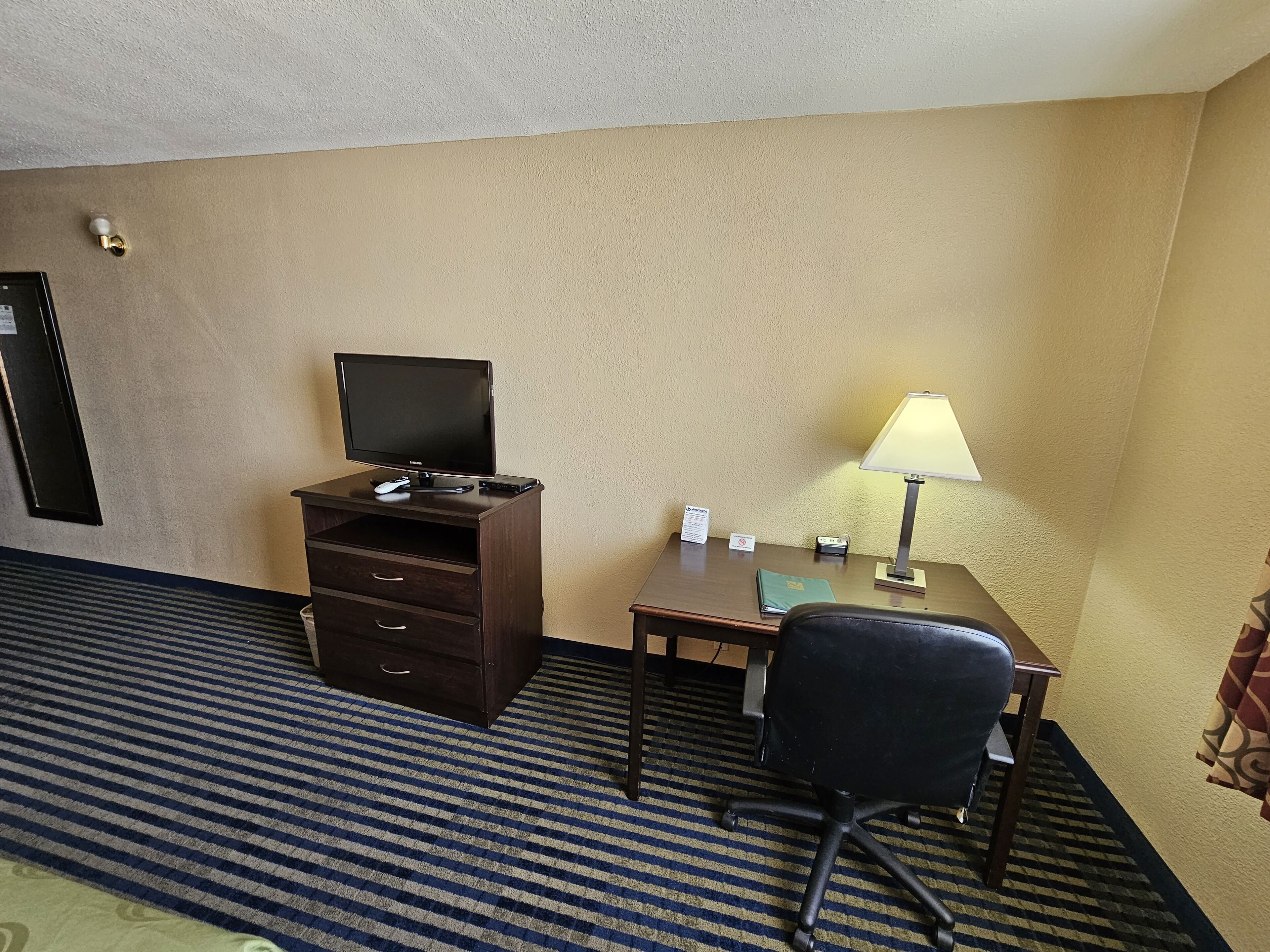 Een hotelkamer met een bureau, stoel, televisie, lamp en een klein kluisje.