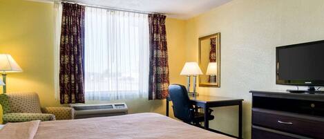 Una habitación de hotel con una cama grande, un escritorio con silla, televisor y ventana con cortinas.