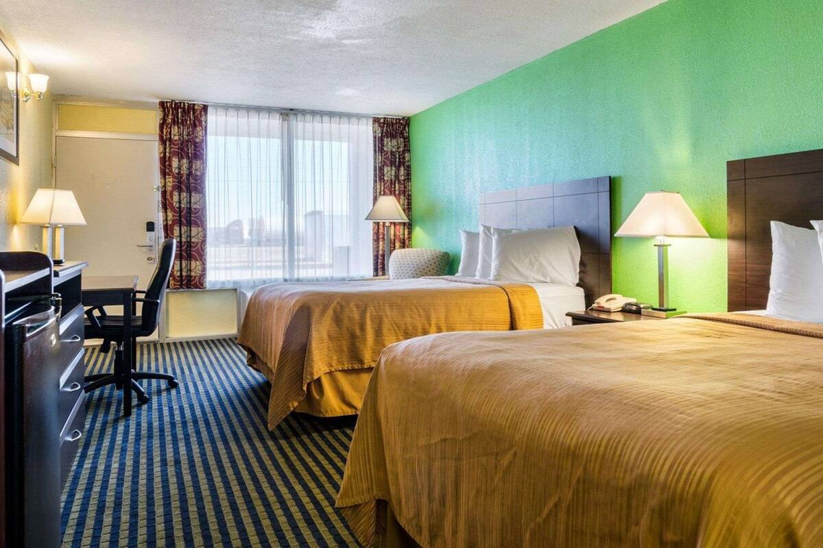 Quarto de hotel com duas camas, uma escrivaninha e uma cadeira.