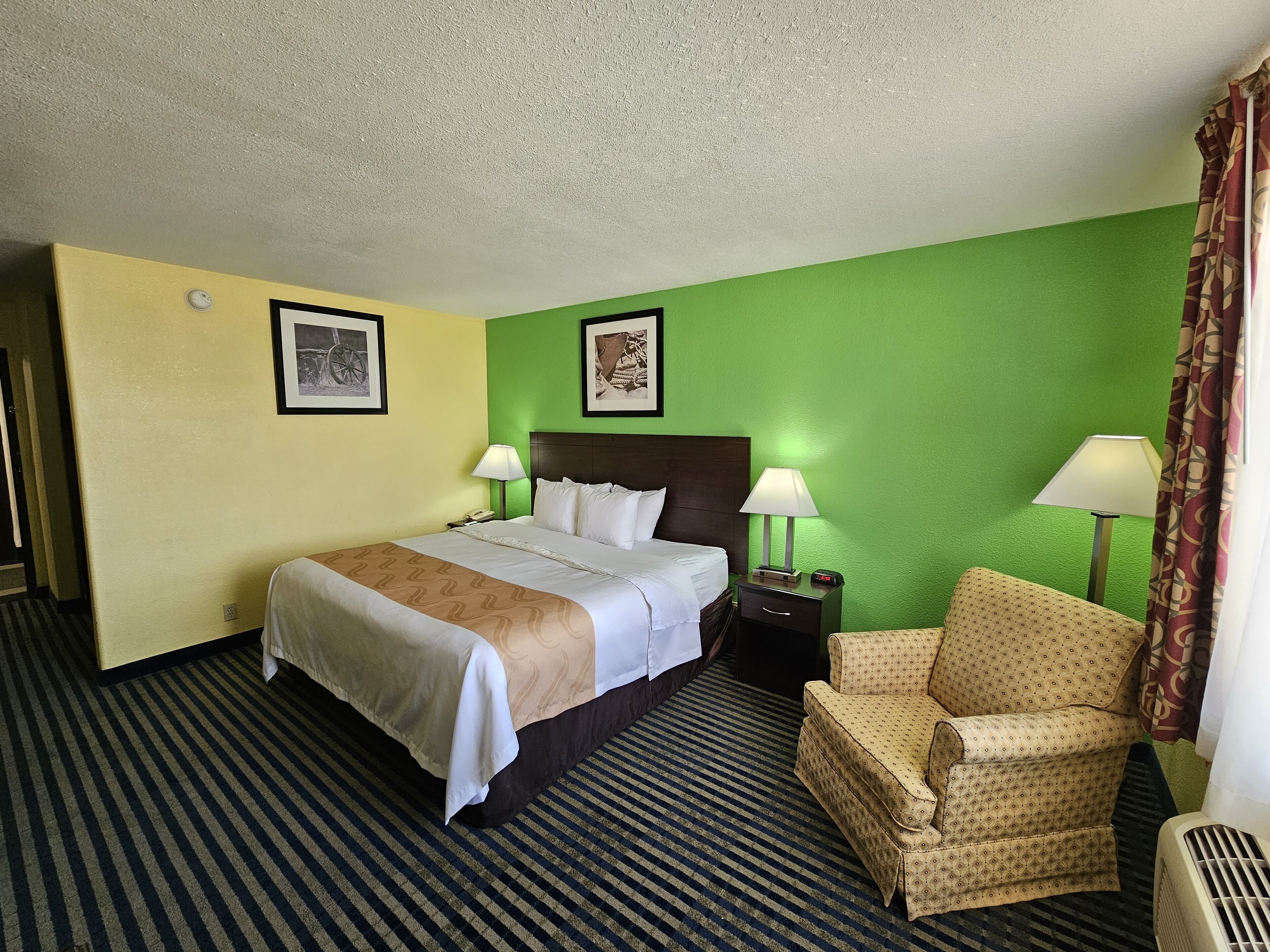 A hotel room with a bed, two bedside tables with lamps, a chair, and a wall with two framed pictures.