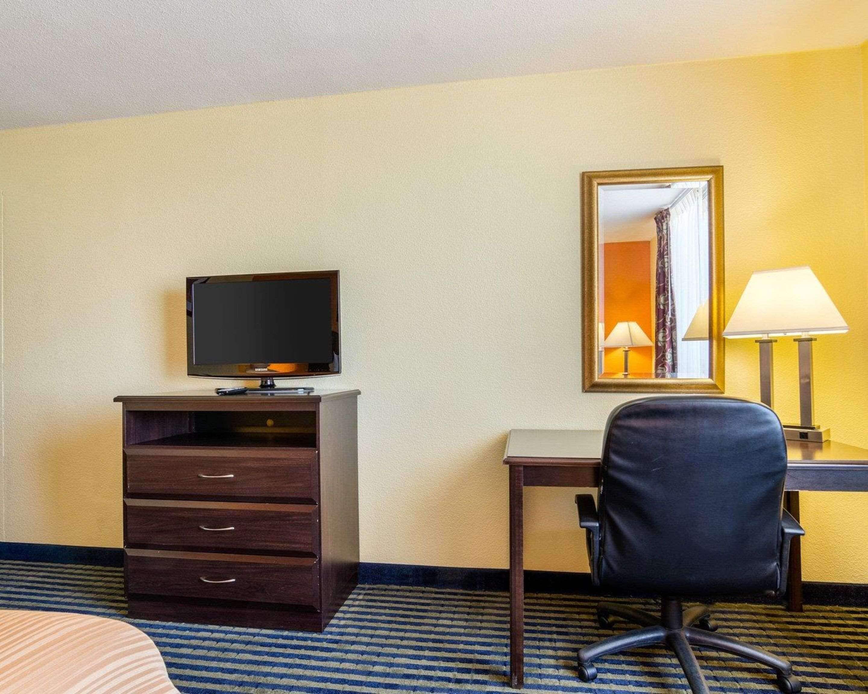 Ein Hotelzimmer mit Bett, Schreibtisch mit Stuhl, Fernseher, Spiegel und Lampe.