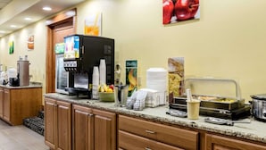 Una barra de desayuno con máquinas de café, un frutero y una estación de comida caliente.