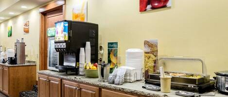 A breakfast bar with coffee machines, a fruit bowl, and a hot food station.