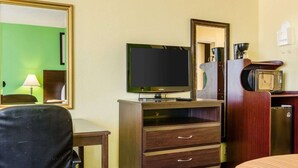Habitación de hotel con televisión, cómoda de madera con cajones, escritorio con lámpara, cama y microondas.