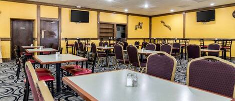 A dining area with multiple tables and chairs, a patterned carpet, and a yellow wall with decorative elements.