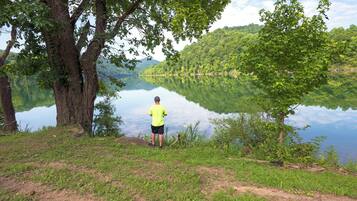 A man standing by a calm lake surrounded by trees.