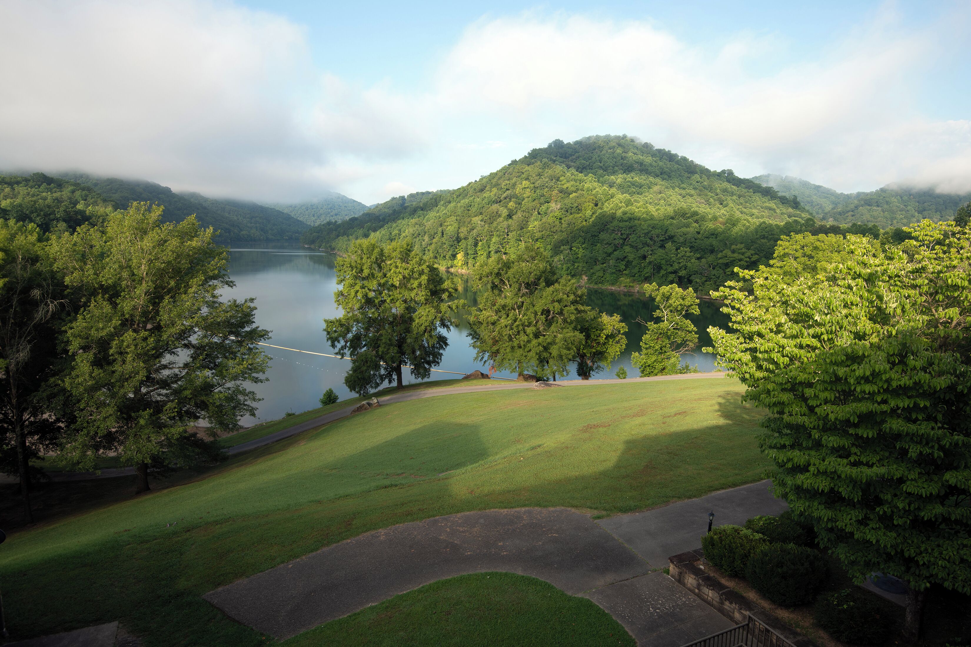 A serene landscape with a lake, lush greenery, and a hilly backdrop.