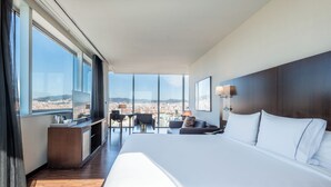 A hotel room with a large bed, a desk, a chair, and a view of the city. - Leonardo Royal Hotel Barcelona Forum (Barcelona)