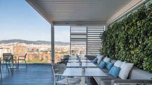 A rooftop terrace with a view of the city, furnished with tables and chairs, and a green wall. - Leonardo Royal Hotel Barcelona Forum (Barcelona)