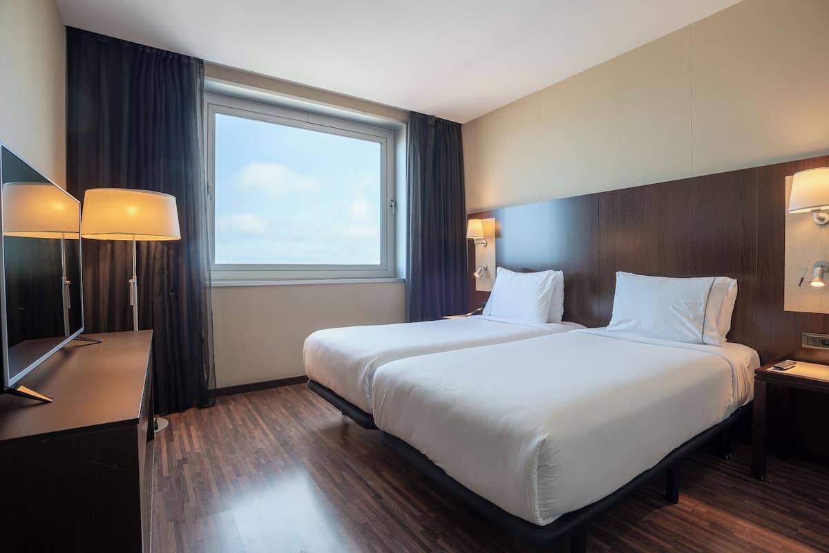 A hotel room with a large bed, two bedside lamps, a flat-screen TV, and a window with curtains.