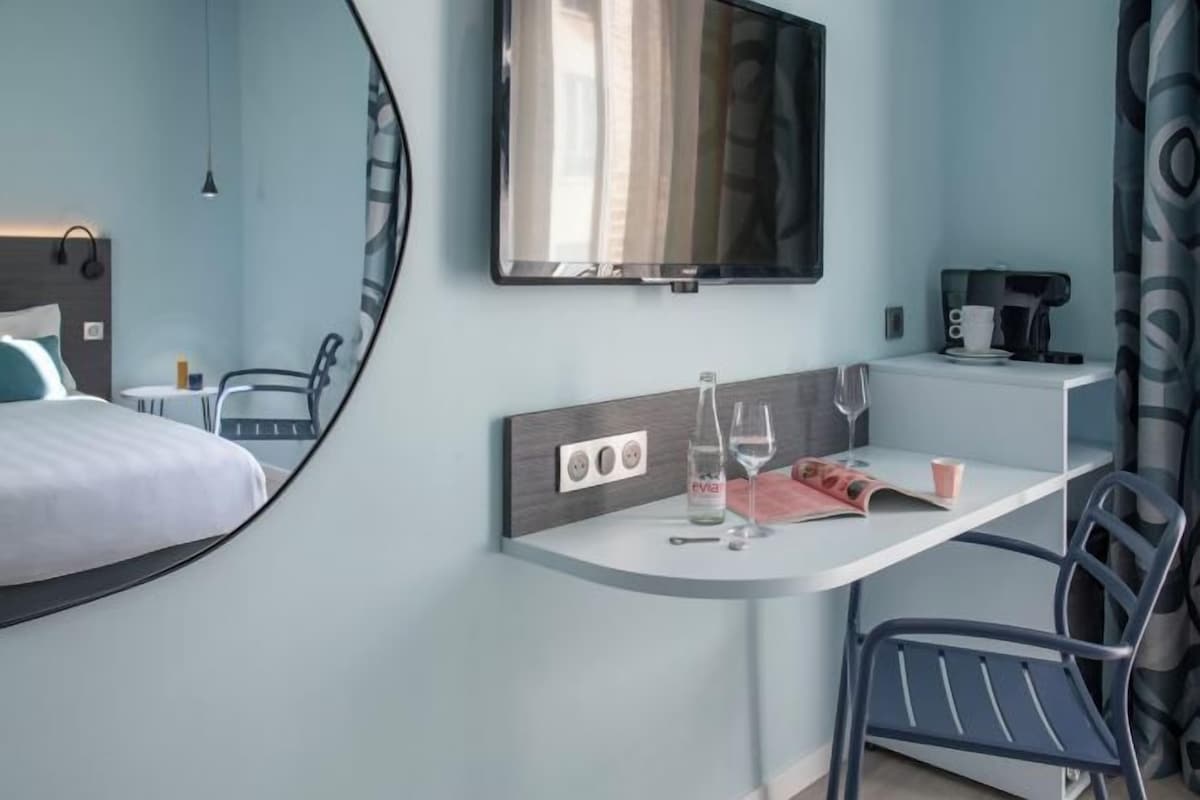A hotel room with a bed, a desk with a chair, a TV, a coffee maker, and a mirror.