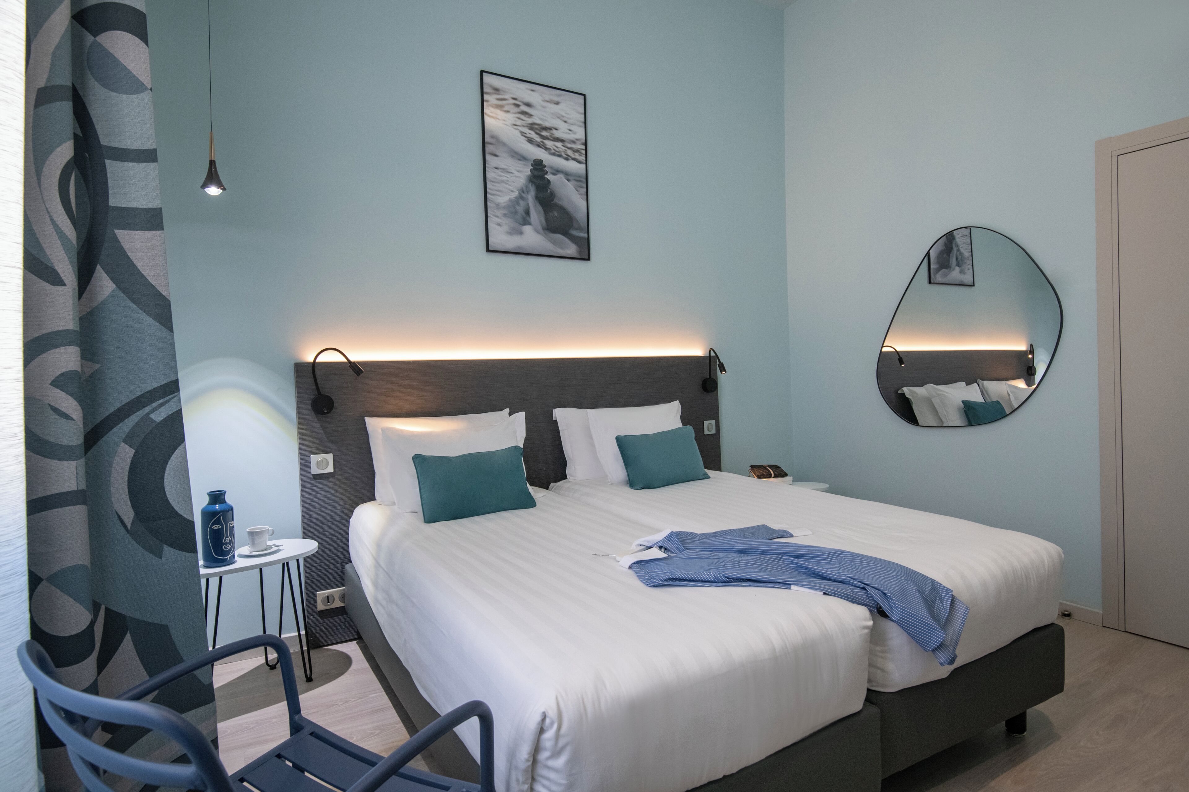 Une chambre d’hôtel moderne avec un grand lit, une table de chevet, une chaise, un miroir fixé au mur et un tableau accroché au mur.