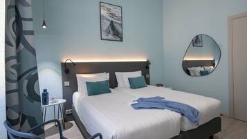 Une chambre d’hôtel moderne avec un grand lit, une table de chevet, une chaise, un miroir fixé au mur et un tableau accroché au mur.