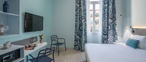 Habitación de hotel con cama, escritorio y silla, televisor y ventana con cortinas estampadas.
