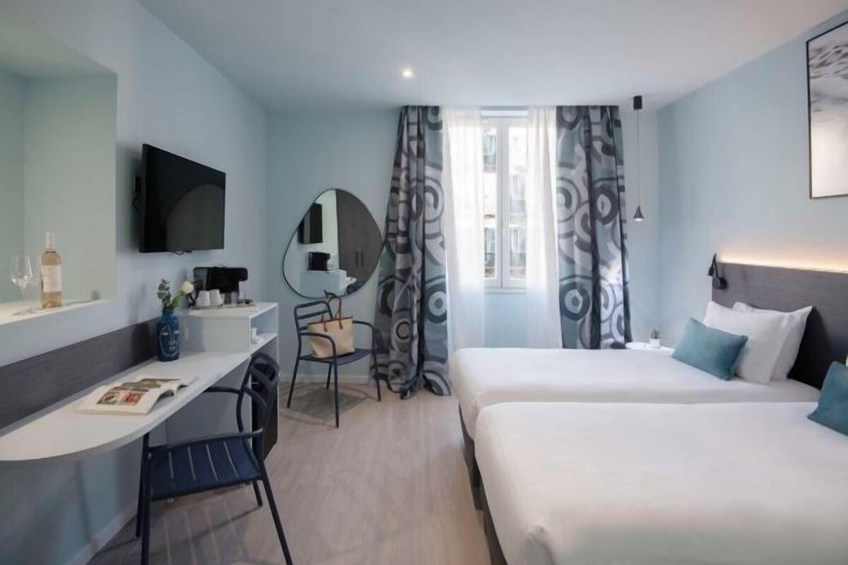 Een moderne hotelkamer met een bureau, twee bedden, een televisie en een raam met gordijnen met een patroon.