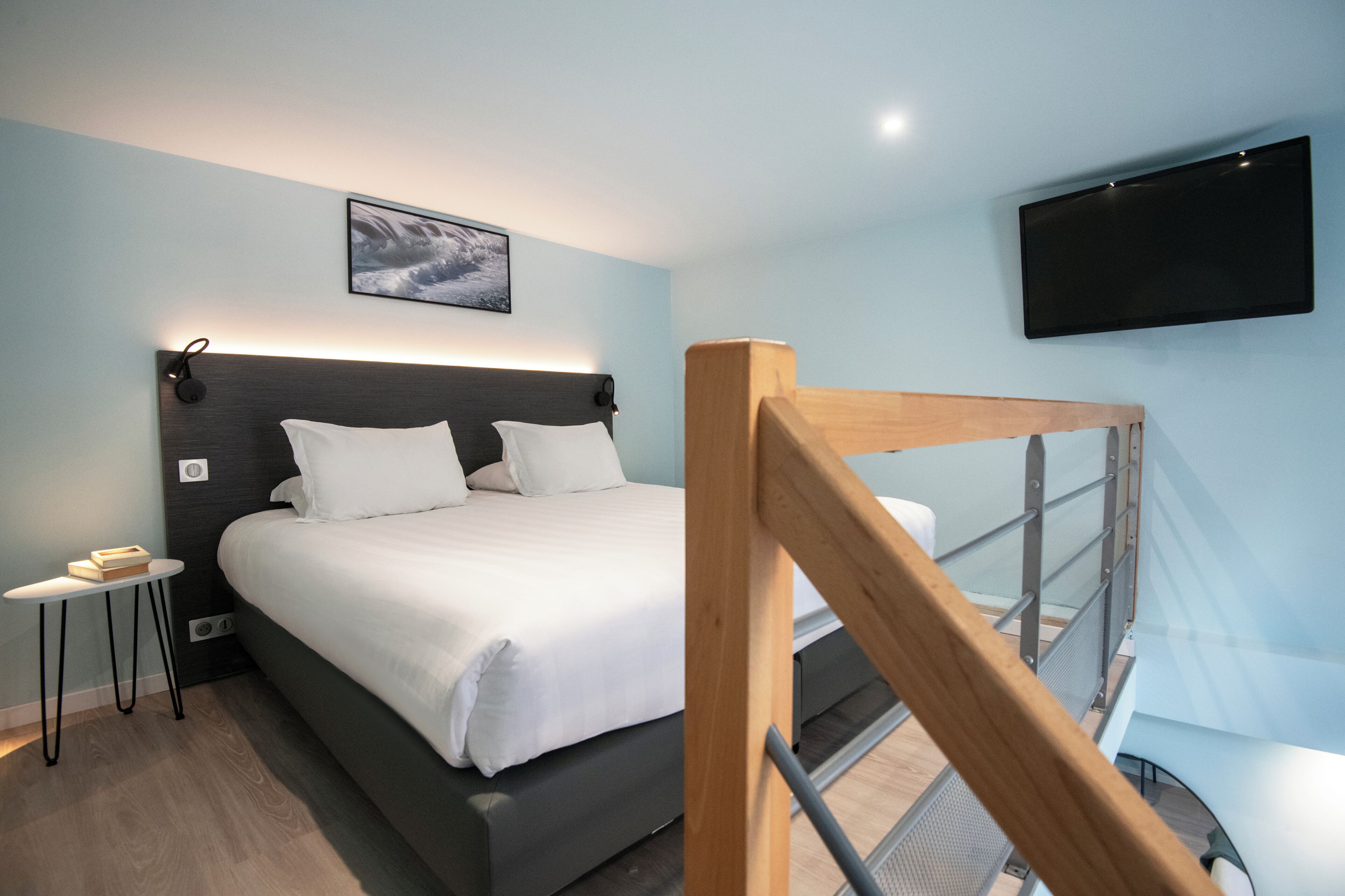 A modern hotel room with a large bed, a bedside table, a mounted TV, and a staircase.