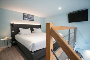 Una habitación de hotel moderna con una cama grande, una mesita de noche, un televisor montado y una escalera.