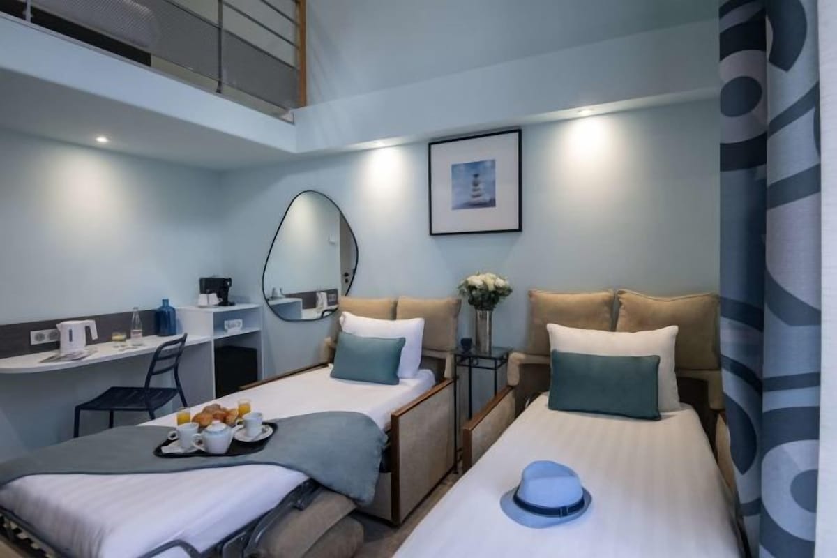 A modern hotel room with two beds, a desk, a chair, a coffee maker, and a breakfast tray.