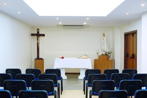 Interior de una iglesia con hileras de sillas, un crucifijo, una estatua y un atril.