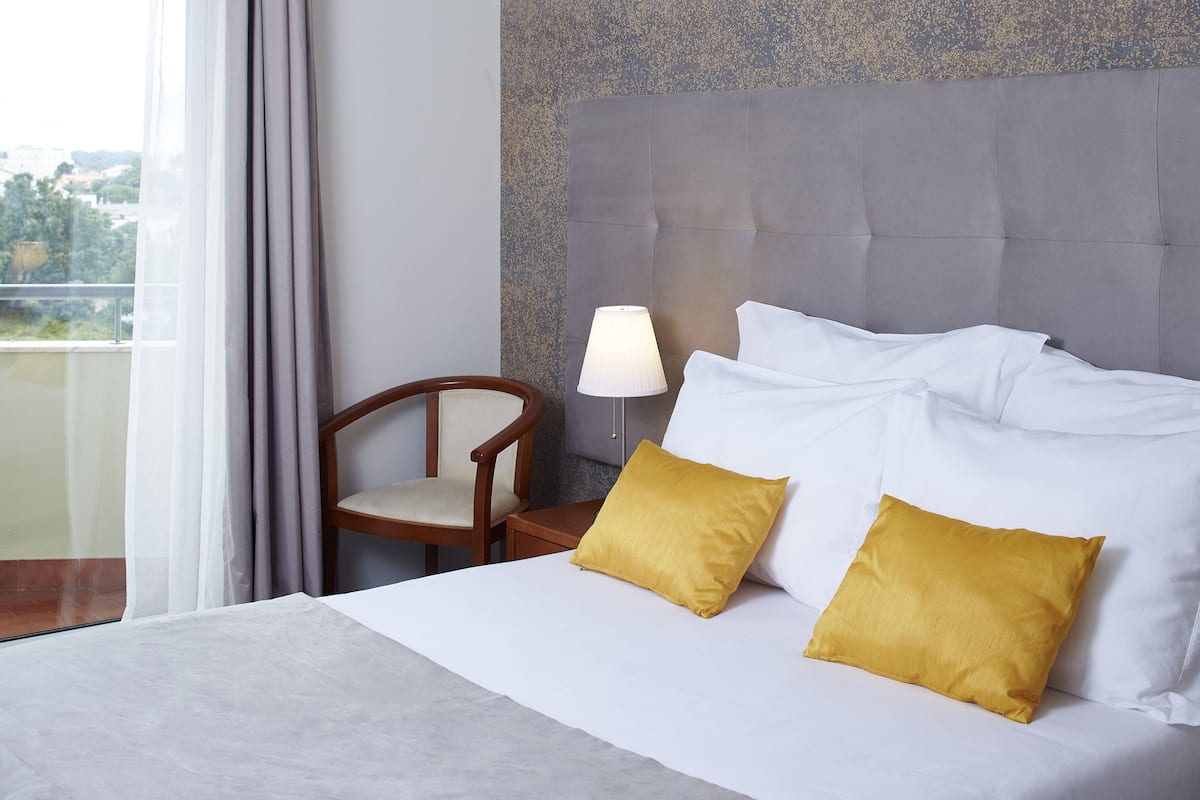 Una camera d'albergo con un letto, due cuscini, un comodino, una lampada, una sedia e vista sull'esterno.