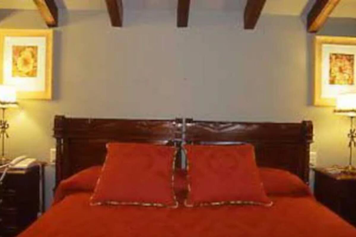 A hotel room with a wooden headboard, two bedside lamps, and a red bedspread.