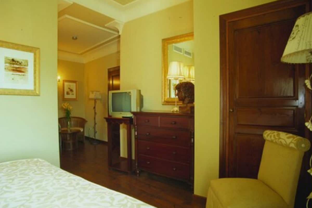 A hotel room with a bed, a wooden dresser, a television, a chair, and a mirror.