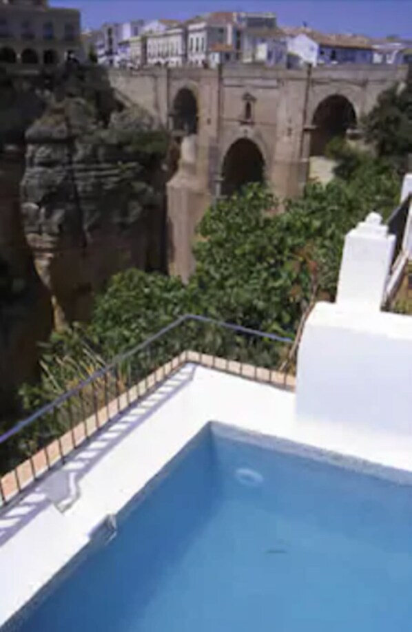 A pool area with a stone bridge in the background. - Hotel Montelirio (Ronda)
