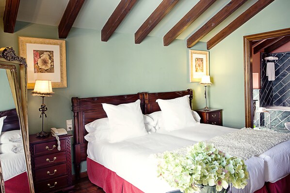 A well-appointed bedroom with a large bed, wooden headboard, a dresser with drawers, a mirror, and two framed artworks on the wall. - Hotel Montelirio (Ronda)