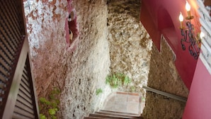 Una escalera con un muro de piedra, una planta en maceta y una pared roja con un portavelas.