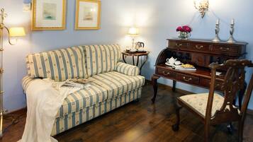 A room with a striped sofa, a wooden side table with a lamp, a wooden chair, and a dresser with a vase of flowers.