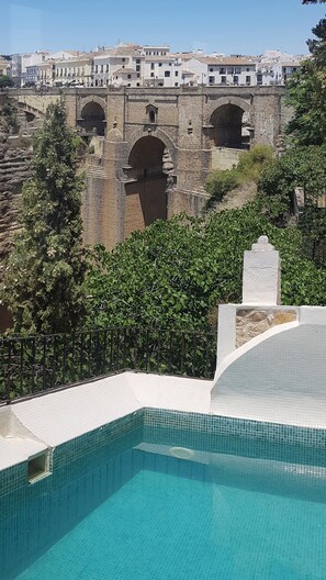 A swimming pool with a view of a historic stone bridge and buildings in the background. - Hotel Montelirio (Ronda)