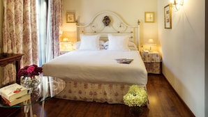 Una cama bien hecha con sábanas blancas, una mesita de noche con una lámpara y un florero con flores.