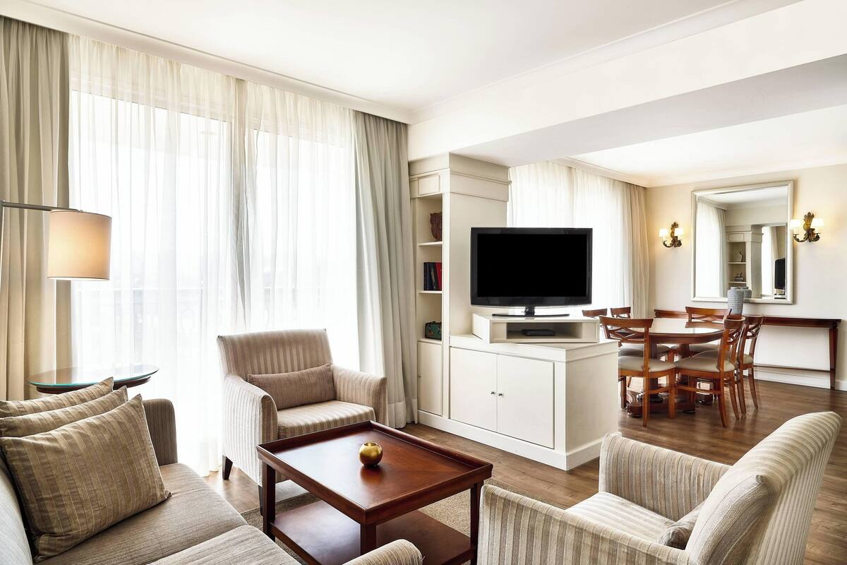 Una sala de estar bien iluminada con sofá, sillones, una mesa de centro, televisor y un comedor con sillas y mesa.