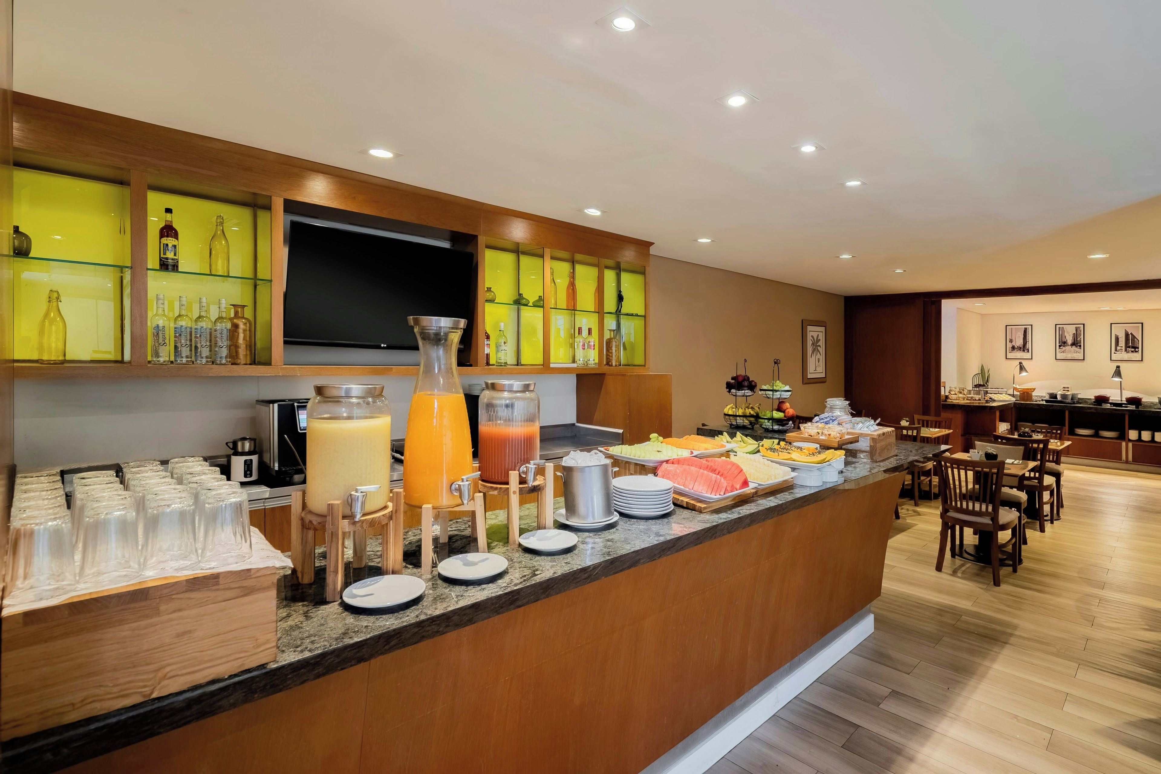 Un espace pour le petit-déjeuner à l’hôtel, comprenant un buffet, un téléviseur à écran plat et un coin repas avec des chaises et des tables.