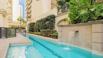 Une piscine agrémentée d’une cascade, entourée de verdure et de bâtiments modernes.
