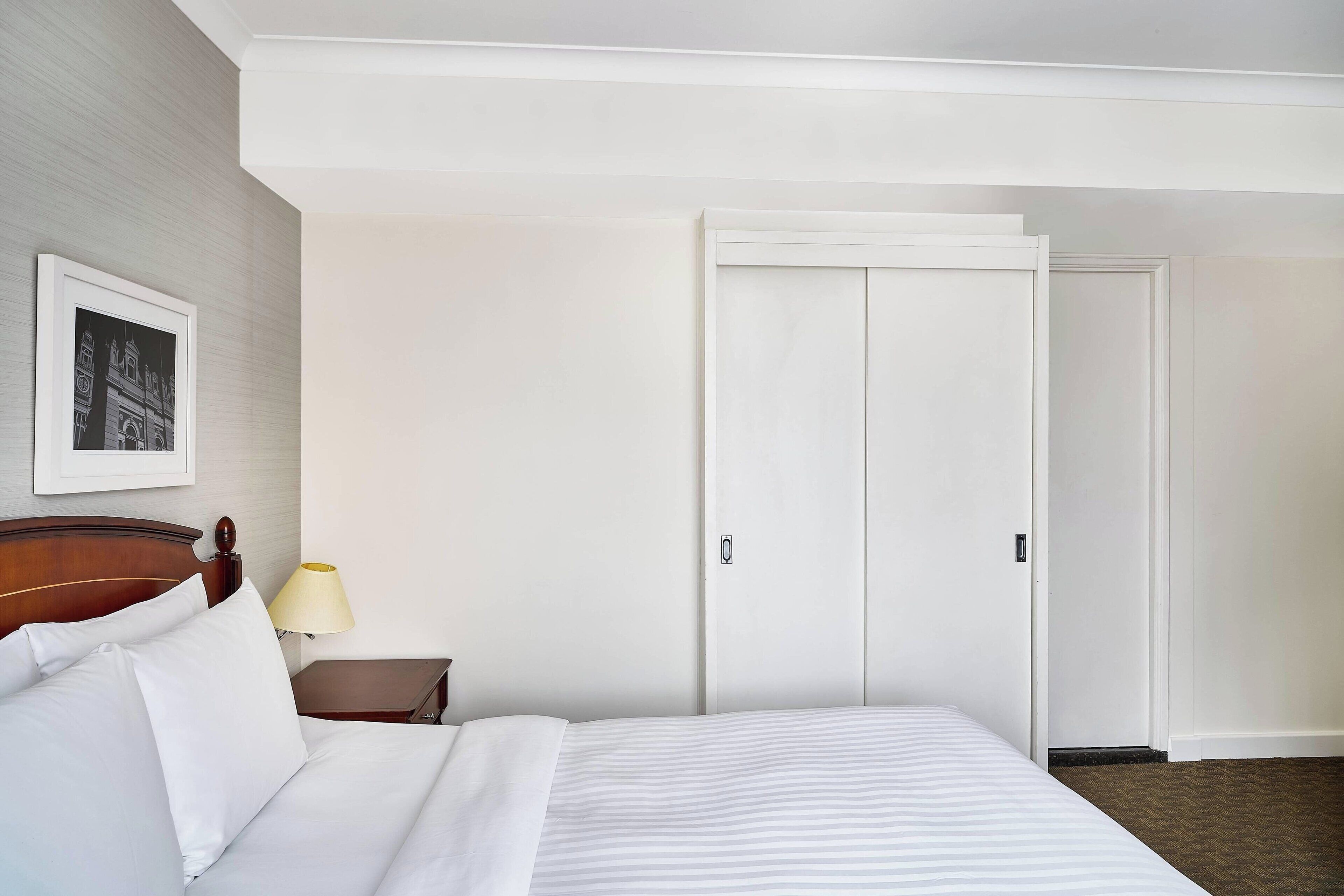 Una habitación de hotel con cama, mesita de noche, lámpara y puerta.