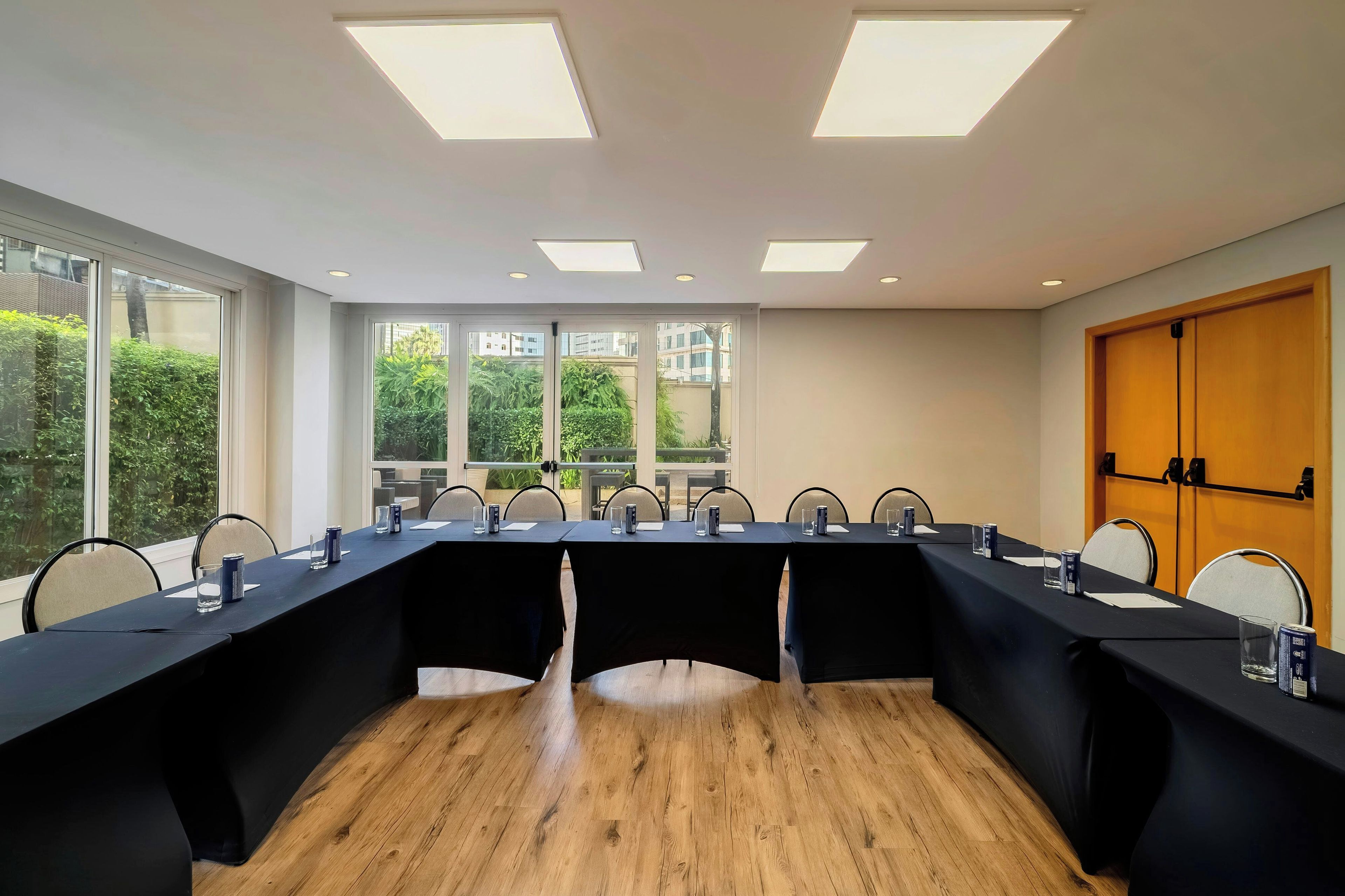 Una sala conferenze con un lungo tavolo, sedie e ampie finestre che offrono vista su aree verdi ed edifici.