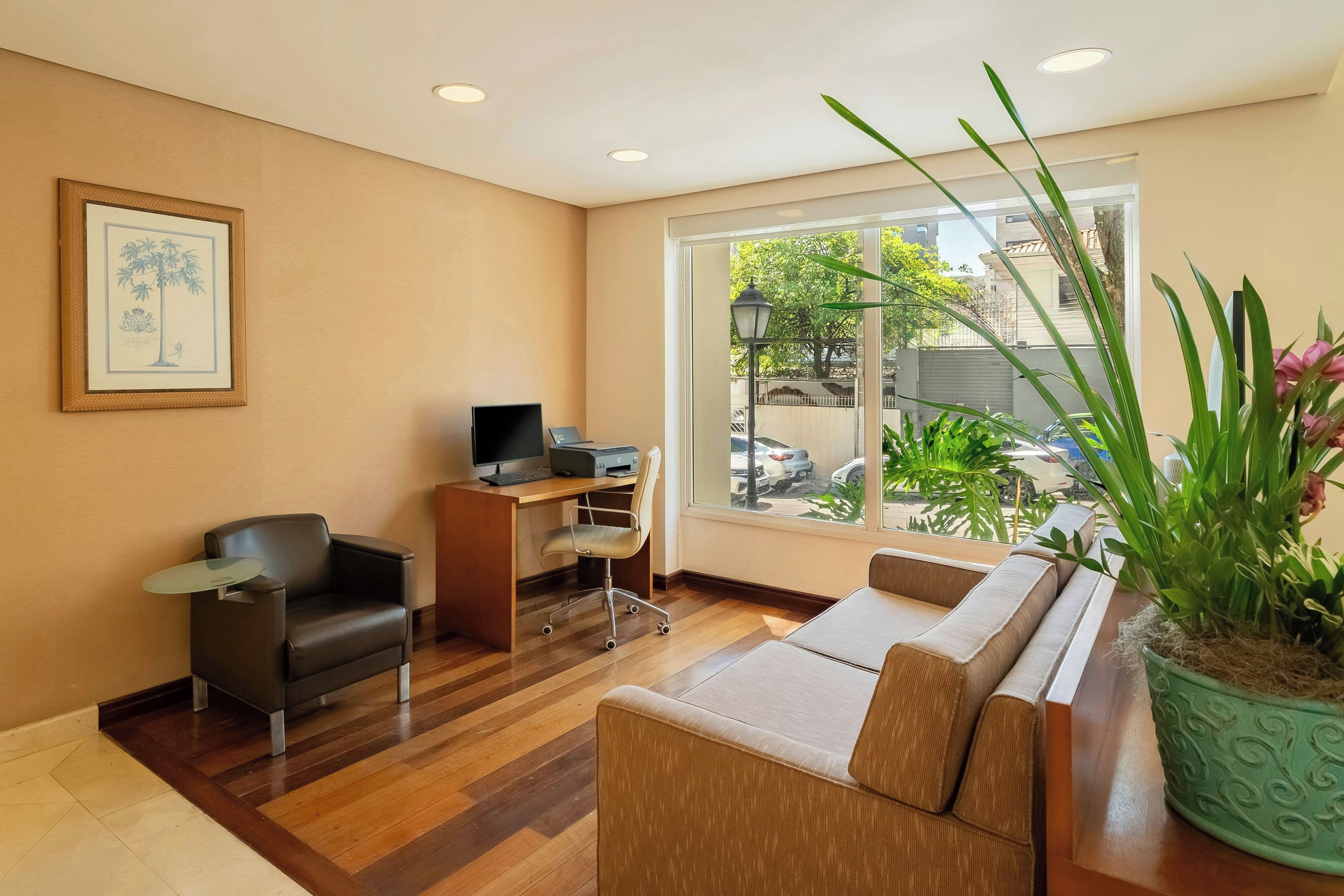 A modern living room with a sofa, a desk with a computer, a chair, and a large window with a view of the outside.