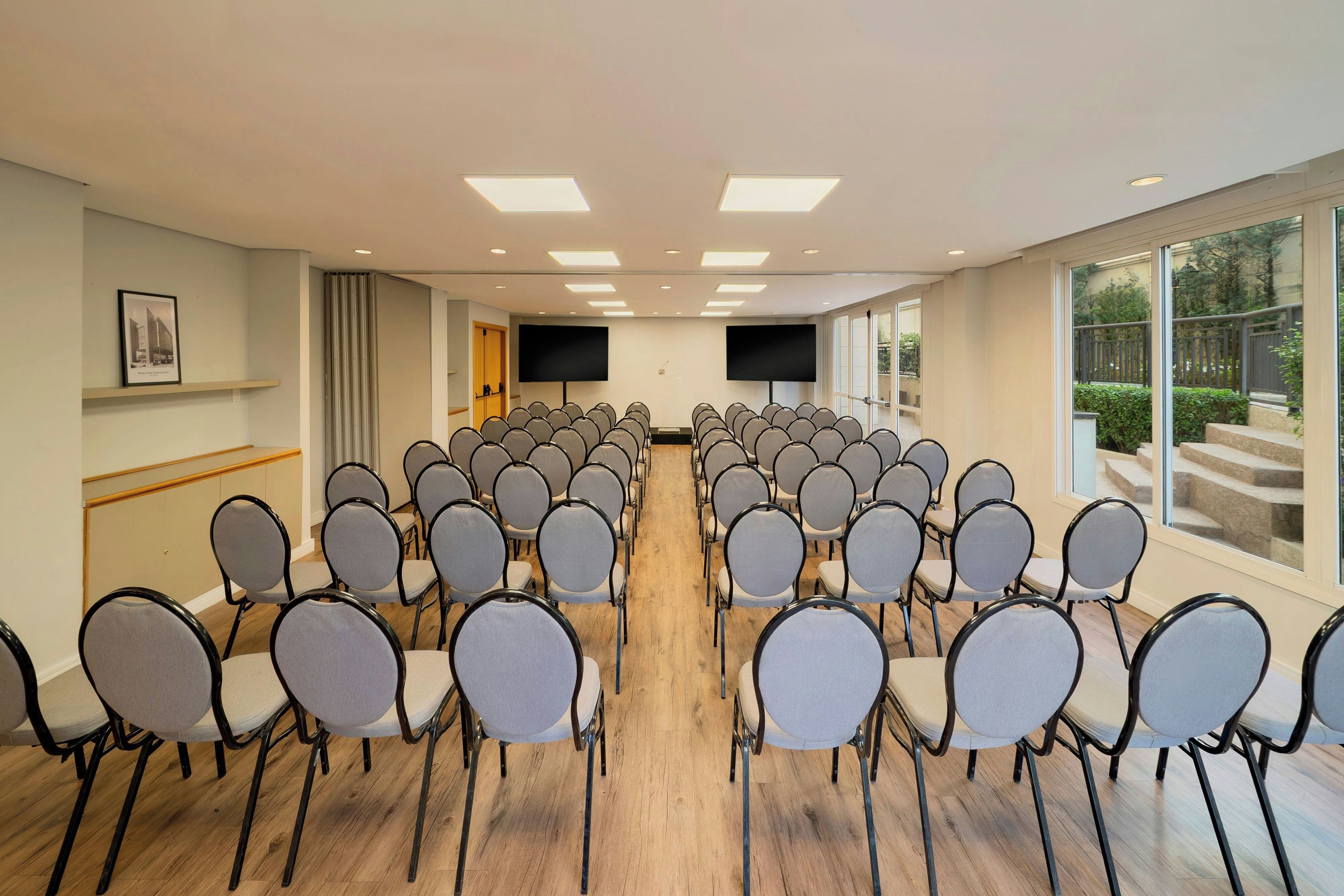 Une salle de conférence avec des rangées de chaises, un grand écran et un plancher en bois.