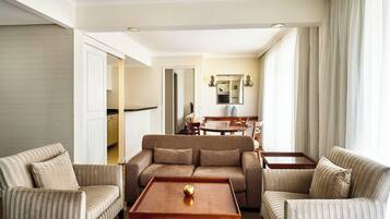 Une chambre d’hôtel avec un canapé à rayures, une table basse en bois agrémentée d’un objet décoratif, et une vue sur la salle à manger par une porte ouverte.