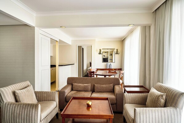 A hotel room with a striped sofa set, a wooden coffee table with a decorative item, and a view of the dining area through an open door.