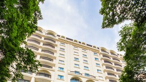 Un hotel de varios pisos con balcones, una entrada de ladrillo rojo y un coche estacionado frente a él.