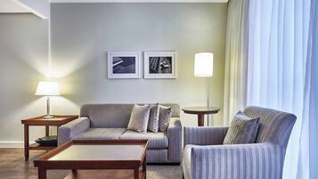 A modern living room with a sofa, armchair, coffee table, and two side tables. There are two framed pictures on the wall and a lamp on one of the side tables.