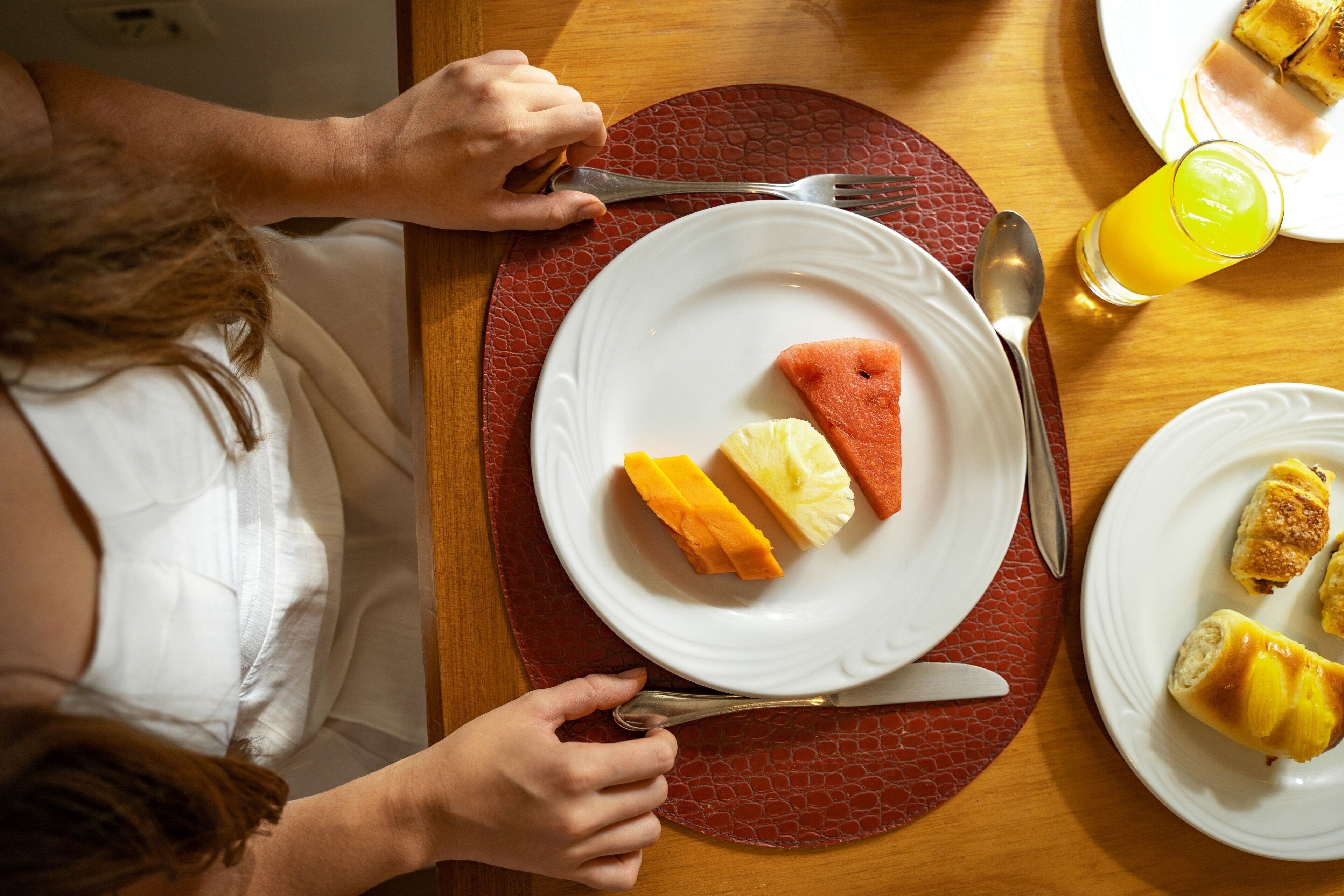 Une table à manger avec une assiette de nourriture, un verre de jus d’orange, une fourchette et un couteau.