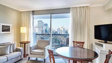 Une chambre d’hôtel avec un balcon, un canapé, un fauteuil, une table à manger et un téléviseur.