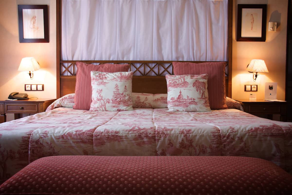 Una cama bien hecha con una colcha floral, dos lámparas de noche y una mesita de noche con un teléfono.